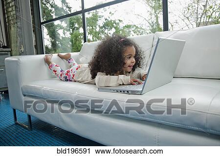 Stock Image - Mixed race girl using laptop on sofa. Fotosearch