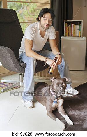Stock Photo - Mixed race man drinking beer and sitting with dog. Fotosearch