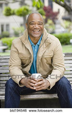 Stock Photograph - Mixed race man drinking coffee in park. Fotosearch