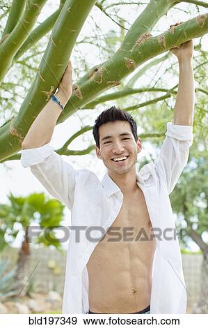 Stock Photo - Mixed race man holding onto tree branch. Fotosearch