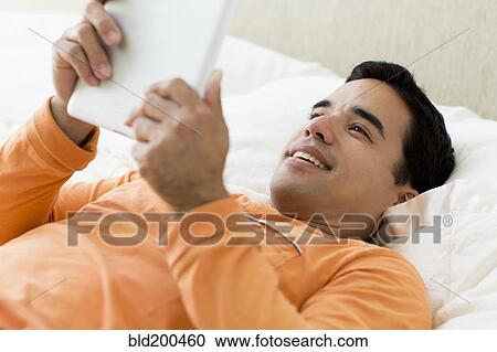 Mixed race man laying in bed using digital tablet View Large Photo Image Stock Image - Mixed race man laying in bed using digital tablet. Fotosearch