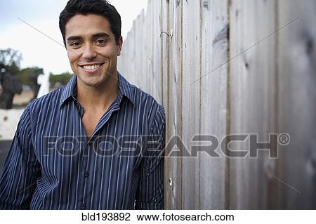 Stock Image - Mixed race man leaning against fence. Fotosearch