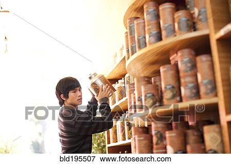 Stock Photo - Mixed race man lifting canister from shelf in shop. Fotosearch