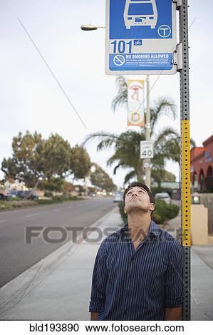 Stock Image - Mixed race man looking at bus stop sign. Fotosearch