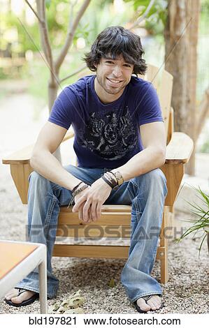 Stock Image - Mixed race man sitting in Adirondack chair. Fotosearch