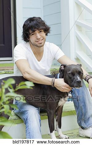 Stock Photo - Mixed race man sitting on front stoop with dog. Fotosearch