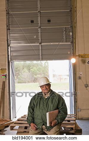 Stock Image - Mixed race man sitting on pallets in warehouse. Fotosearch