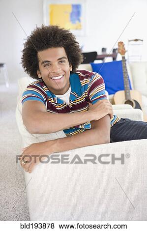 Stock Photo - Mixed race man sitting on sofa. Fotosearch