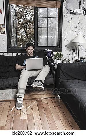 Stock Image - Mixed race man sitting on sofa with laptop. Fotosearch