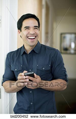 Stock Image - Mixed race man text messaging on cell phone. Fotosearch