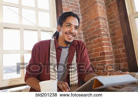 Stock Photo - Mixed race man using digital tablet in coffee shop. Fotosearch