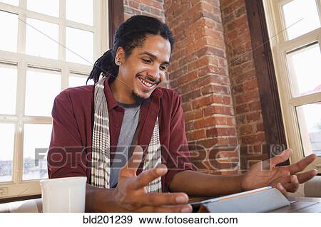 Stock Photo - Mixed race man using digital tablet in coffee shop. Fotosearch