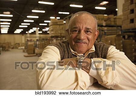 Stock Image - Mixed race man with arms crossed in warehouse. Fotosearch