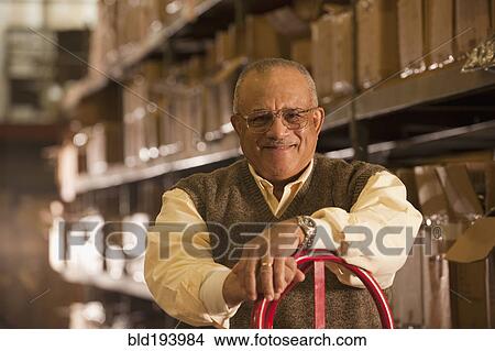 Picture - Mixed race man with hand truck in warehouse. Fotosearch