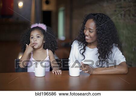 Stock Photograph - Mixed race mother and daughter drinking hot chocolate. Fotosearch