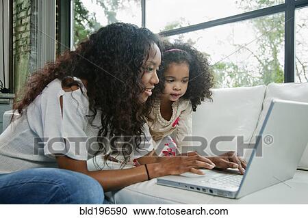 Stock Image - Mixed race mother and daughter using laptop together. Fotosearch