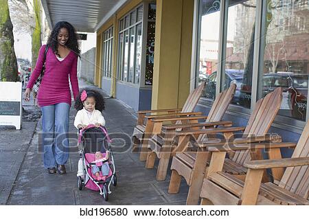 Stock Image - Mixed race mother and daughter walking on sidewalk. Fotosearch