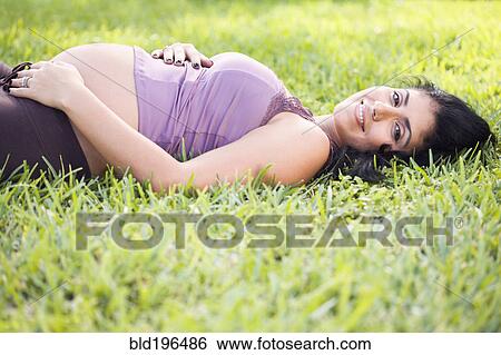Stock Photograph - Mixed race pregnant woman laying in grass. Fotosearch