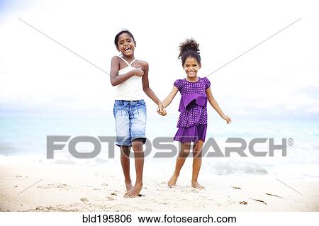 Stock Photograph - Mixed race sisters holding hands on beach. Fotosearch