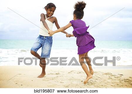 Stock Photo - Mixed race sisters holding hands playing on beach. Fotosearch