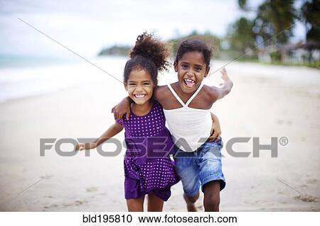 Stock Image - Mixed race sisters hugging on beach. Fotosearch