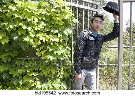 Stock Image - Mixed race teenage boy leaning against gate and looking serious. Fotosearch