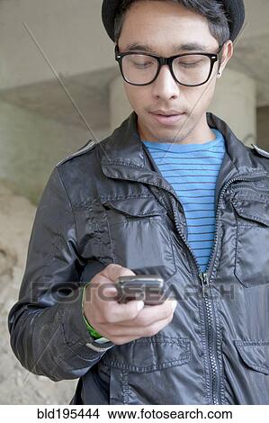 Picture - Mixed race teenage boy text messaging with cell phone. Fotosearch