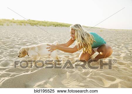 Stock Photography - Mixed race teenage girl playing with puppy on beach. Fotosearch