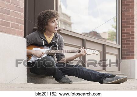 Stock Image - Mixed race teenager playing electric guitar and singing. Fotosearch