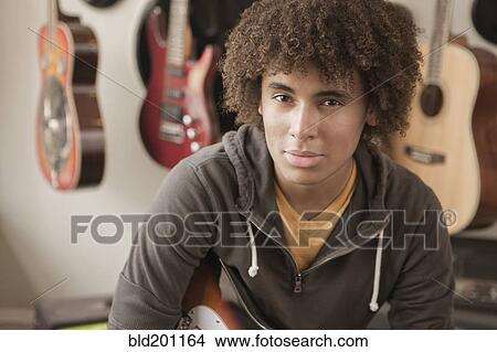 Picture - Mixed race teenager sitting with guitars. Fotosearch