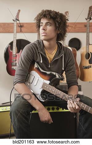 Stock Image - Mixed race teenager sitting with electric guitar. Fotosearch