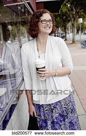 Stock Photo - Mixed race woman drinking coffee on sidewalk. Fotosearch