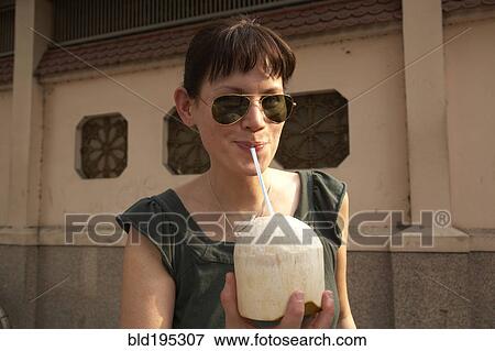 Stock Photo - Mixed race woman drinking from coconut. Fotosearch