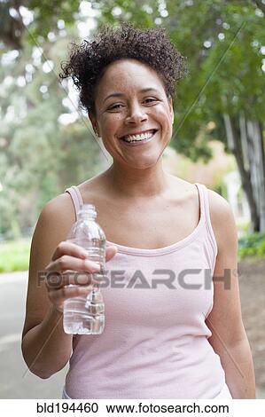 Stock Image - Mixed race woman drinking water in park. Fotosearch
