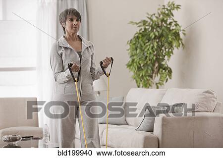 Stock Image - Mixed race woman exercising in living room. Fotosearch