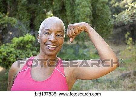 Stock Photograph - Mixed race woman flexing muscles outdoors. Fotosearch