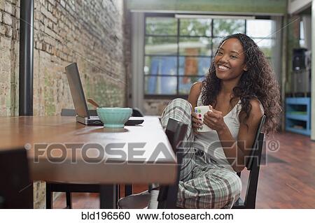 Stock Image - Mixed race woman having breakfast and using laptop. Fotosearch