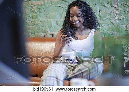 Stock Image - Mixed race woman having breakfast and using cell phone. Fotosearch