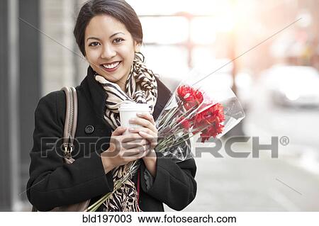 Stock Image - Mixed race woman holding coffee and bouquet of flowers. Fotosearch