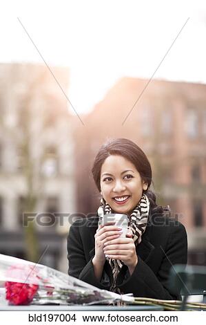 Picture - Mixed race woman holding coffee with bouquet of flowers. Fotosearch