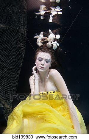 Stock Image - Mixed race woman in dress swimming under water. Fotosearch