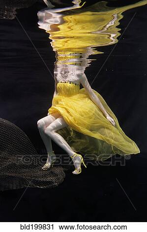 Stock Image - Mixed race woman in dress swimming under water. Fotosearch