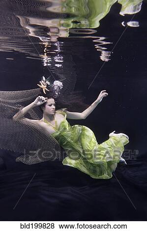Stock Photo - Mixed race woman in dress swimming under water. Fotosearch