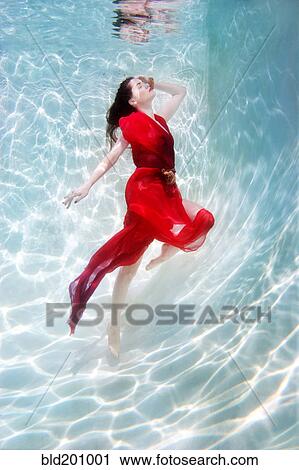 Stock Image - Mixed race woman in dress underwater in swimming pool. Fotosearch