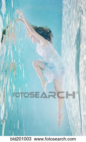 Stock Image - Mixed race woman in dress underwater in swimming pool. Fotosearch