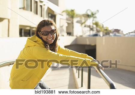 Stock Image - Mixed race woman in sunglasses leaning on railing. Fotosearch