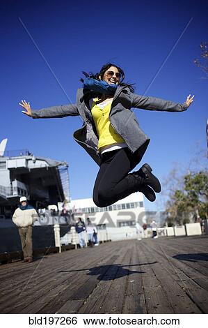Stock Photograph - Mixed race woman jumping on boardwalk. Fotosearch