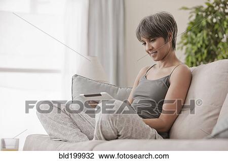 Stock Image - Mixed race woman on sofa using digital tablet. Fotosearch