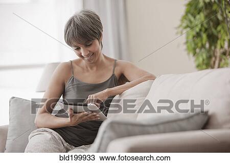 Stock Image - Mixed race woman on sofa using digital tablet. Fotosearch