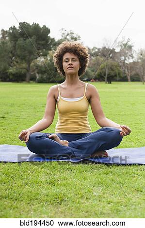 Stock Image - Mixed race woman practicing yoga in park. Fotosearch